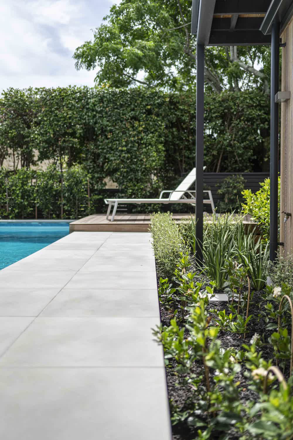 Maintained poolside garden beds with black mulch and hedge